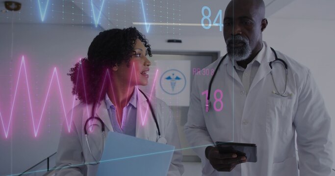 Walking doctors in labcoats reviewing records in hall, showing steths blue folder tablet ECG 84 18