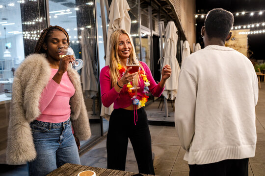 Young diverse friends celebrating and socializing at an outdoor restaurant or bar, enjoying beverages on a festive evening