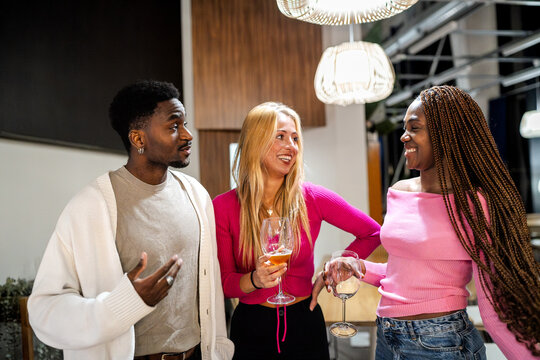 Diverse young friends chatting and clinking wine glasses at a lively urban restaurant party, enjoying nightlife and celebration