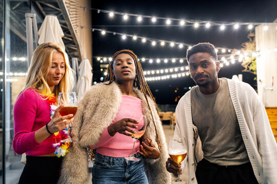 Diverse group of young friends gathering, socializing, and drinking wine and beer at an outdoor restaurant or bar at night