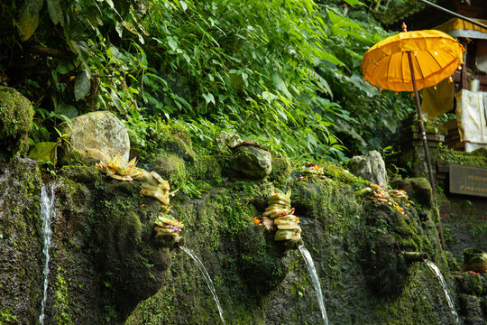 Sacred water pours from stone spouts adorned with traditional offerings
