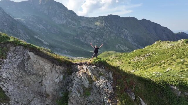 A man standing triumphantly with raised arms on a rocky ridge at Achishkho mountain in Krasnaya Polyana, Sochi, Russia.