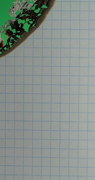 Burning Grid Paper with Green Chroma Key Background. Blue squared paper burns along spreading charred edge against green chroma key. Slow burn creates practical transition element for compositing.