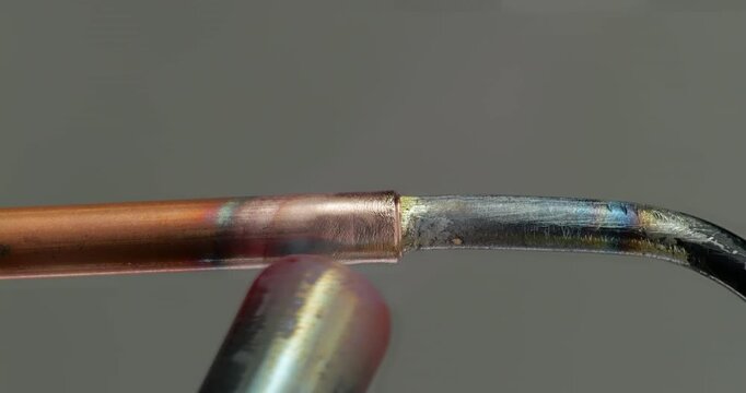 Close Up Repair Soldering on Refrigerator Condenser. Copper tube meets steel condenser tubing as gas torch heats joint. Close up brazing shows filler metal joining household refrigerator components