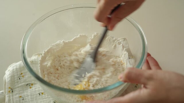 Mixing flour and egg with a black spatula while holding the bowl
