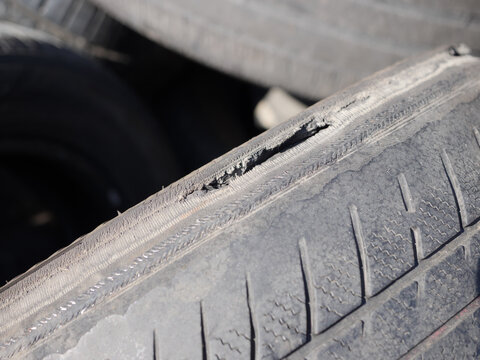 Close-up of a severely worn car tire with damaged shoulder and exposed reinforcing cords. Old tire showing dangerous tread wear and rubber deterioration, highlighting road safety and replacement.