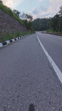 Vertical cycling POV footage on a winding mountain road, passing a stone retaining wall, black and white curb markings and a pickup truck ahead on the asphalt roadway.