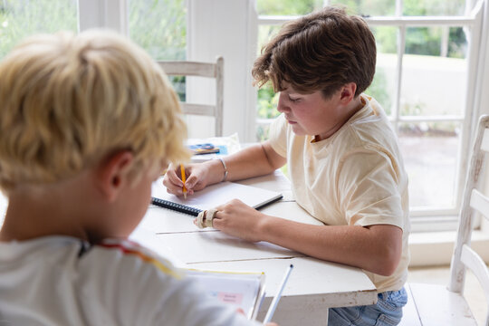 pre teen and early teen boy doing homework together in light filled room