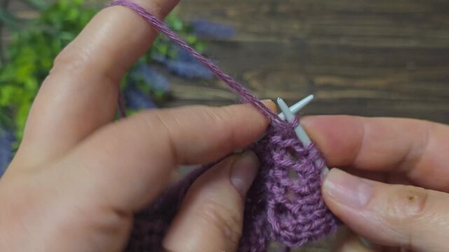 The process of knitting a multicolored openwork yoke for a jumper or cardigan. The raised pattern is on circular needles, and the work is placed on a dark wooden table.