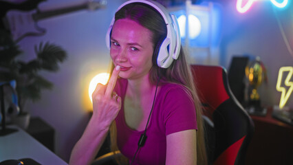 Woman gamer wearing headphones flips middle finger toward camera at gaming desk in studio  defiance attitude. © Krakenimages.com