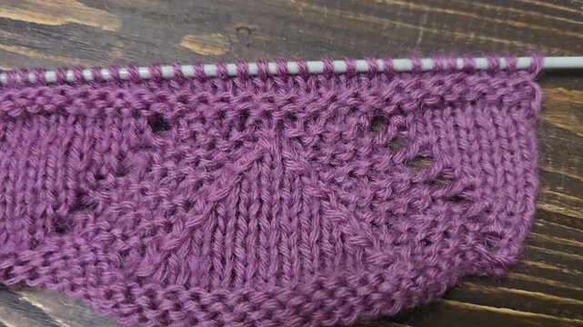 The process of knitting a multicolored openwork yoke for a jumper or cardigan. The raised pattern is on circular needles, and the work is placed on a dark wooden table.