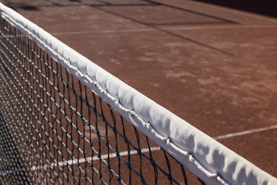 Close up of a white tennis net over a red clay court surface during a sunny day outdoor
