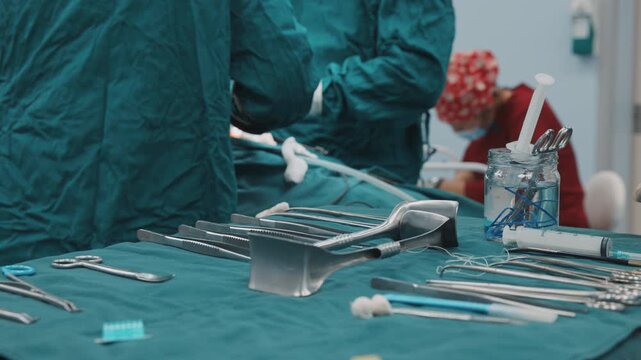 Sterile surgical instruments lie arranged on a covered table while medical staff prepare in the operating room. Surgery preparation, hospital hygiene, instrument setup, clinical workflow