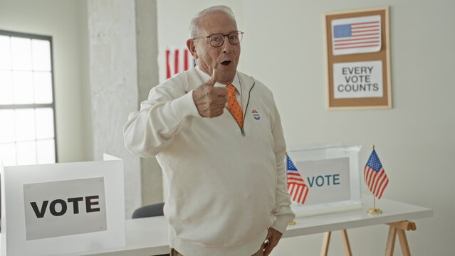 Elderly man gives thumbsup beside a ballot box in a voting building, wearing an orange tie and an i voted sticker while smiling and pointing; civic pride duty.