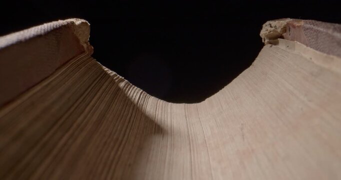 Cinematic closeup pull-back slider movement over an old vintage book on a black background, filmed with a probe lens. Atmospheric lighting highlights aged sheets and timeless character of the book.