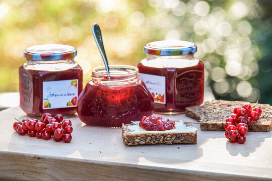 Three jars of red currant jam with seeded bread slices spread with jam