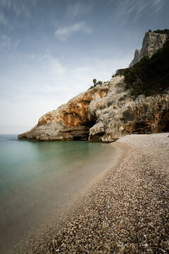 Pebble beach with rocky cliffs at Cala Sisine in Sardinia, Italy