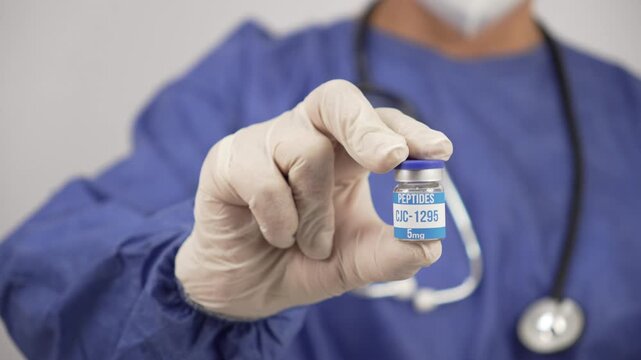Male doctor in blue scrubs and stethoscope holding a vial of cjc-1295 peptides hormone treatment