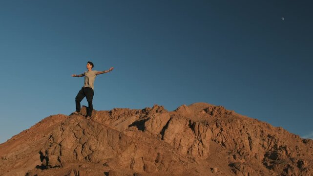 Man standing on a sunlit mountain ridge with arms open to the wind, embracing freedom and a sense of limitless possibility, personal breakthrough and openness to new beginnings in nature