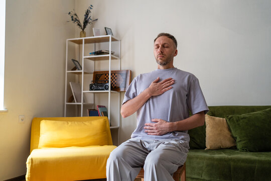 Diaphragmatic breathing exercise for stress relief and relaxation, middle aged man practicing breathwork and mindfulness at home with hands on chest and abdomen