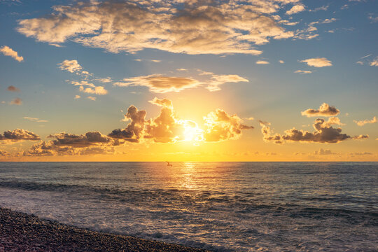 Golden ocean sunset with glowing clouds and sea waves, scenic coastal landscape at golden hour, peaceful nature seascape over pebble beach with dramatic sky