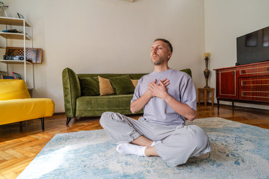 Mindfulness meditation and breathing exercise for stress relief, middle aged man practicing self compassion and emotional wellness at home with hands over heart