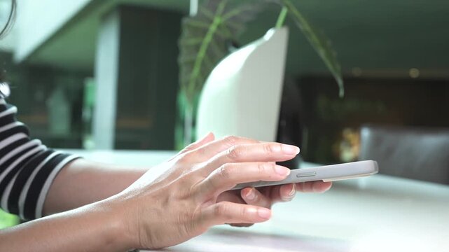 Woman using phone to send text messages or reply to business emails with clients during weekend leisure time at modern cafe.