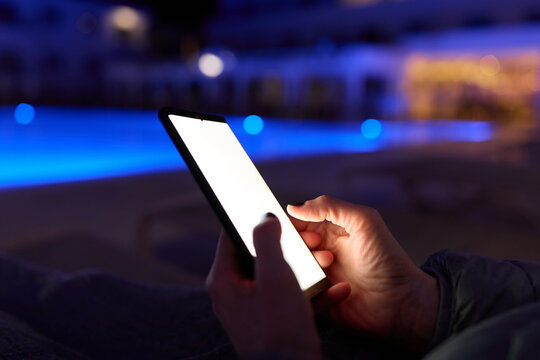 Woman using smartphone by pool at night &ndash; glowing screen, copy space, modern lifestyle