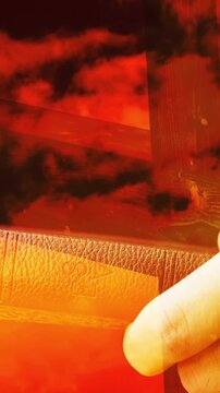Vertical video: Hand entering, holding orange film, shifting, revealing leather, wood, drops