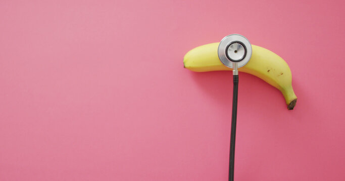 Image of fresh banana with stethoscope with copy space on pink background