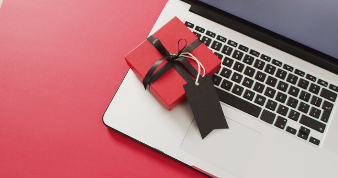 Laptop and red gift box with black ribbon and gift tag, on red background with copy space