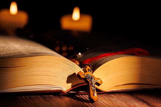 Close up of an open purple bible and white candles with an olive wood rosary for christian prayer and religious devotion and holy faith.