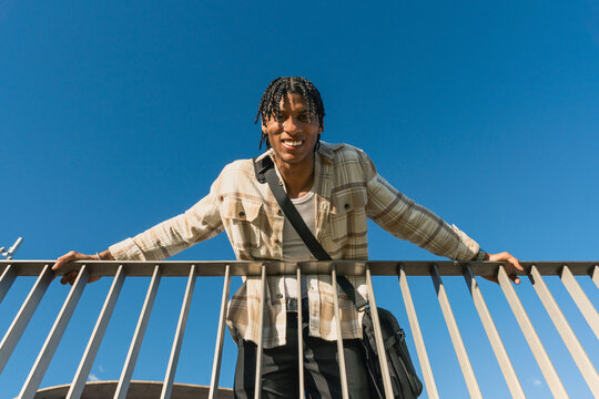 Young cuban student smiling at the camera leans against an outdoor railing
