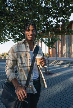 Young black man smiling at the camera while holding coffee cup
