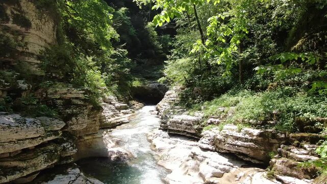 Scenic view of the crystal-clear Khosta River flowing through the deep white rock canyon and lush green forest in Sochi, Russia.