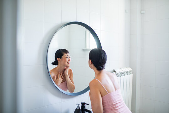 Woman touching her neck while looking in a bathroom mirror