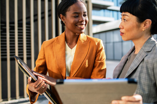 Two businesswomen discussing project on a tablet outdoors