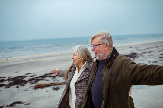 Smiling senior couple walking with arms outstretched on beach