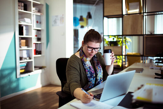 Woman taking notes while working on laptop in office