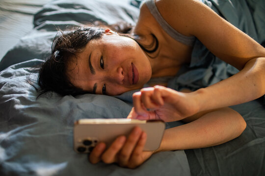 Woman using smartphone in bed at home