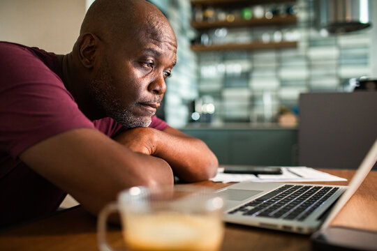 Man leans on table looking at laptop in kitchen