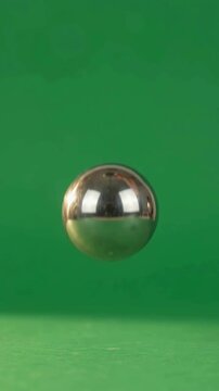 Reflective silver ball bouncing on green surface in natural ambient lighting