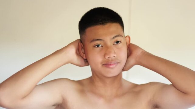Portrait of Asian teenage boy with buzz cut hairstyle, hands on head against white background	