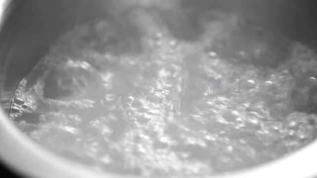 Water boiling vigorously in a metal pot with rising bubbles and steam