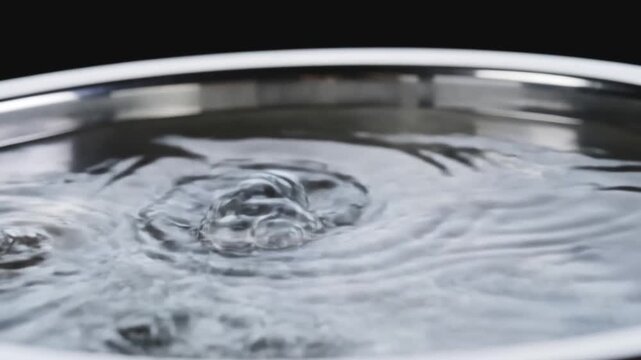 Water rippling and bubbling in a stainless steel pot against black background