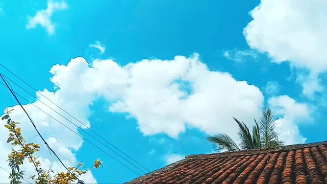 Bright blue sky with fluffy white clouds moving over a tiled rooftop cloud roof weather cumulus sunny