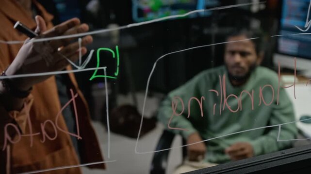 Indian and Asian young adult developers brainstorming software flowchart on glass board in modern office. Clip suitable for corporate technology and startup promotional videos