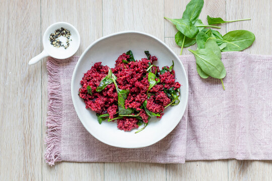 Beetroot risotto with spinach in white bowl on wooden table