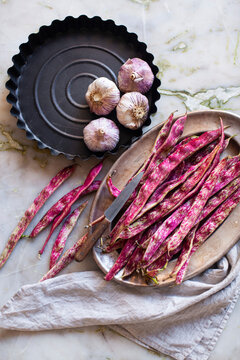Borlotti beans and garlic bulbs displayed on metal plates with a knife