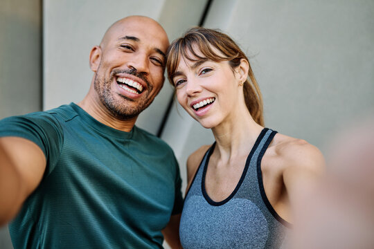 Young couple taking a selfie while posing against a wall after workout in athletic wear at urban location